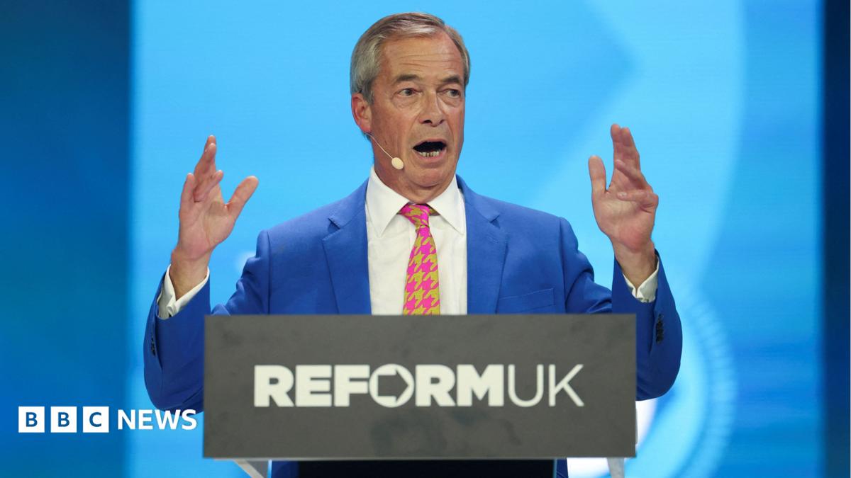 Nigel Farage holds up his hands as he gives his conference speech from behind a podium with Reform UK's logo.