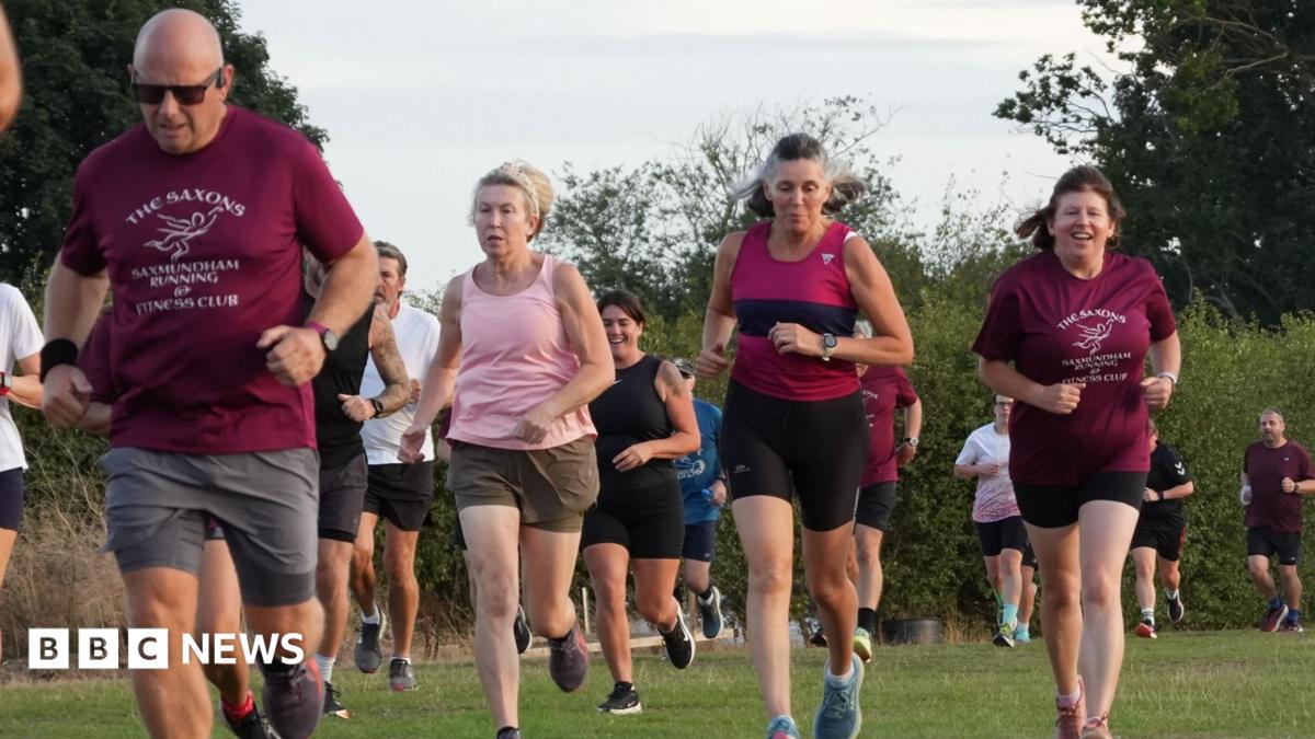 A group of men and women running in a grass field. Some wearing matching maroon coloured T-shirts which are the club colours.