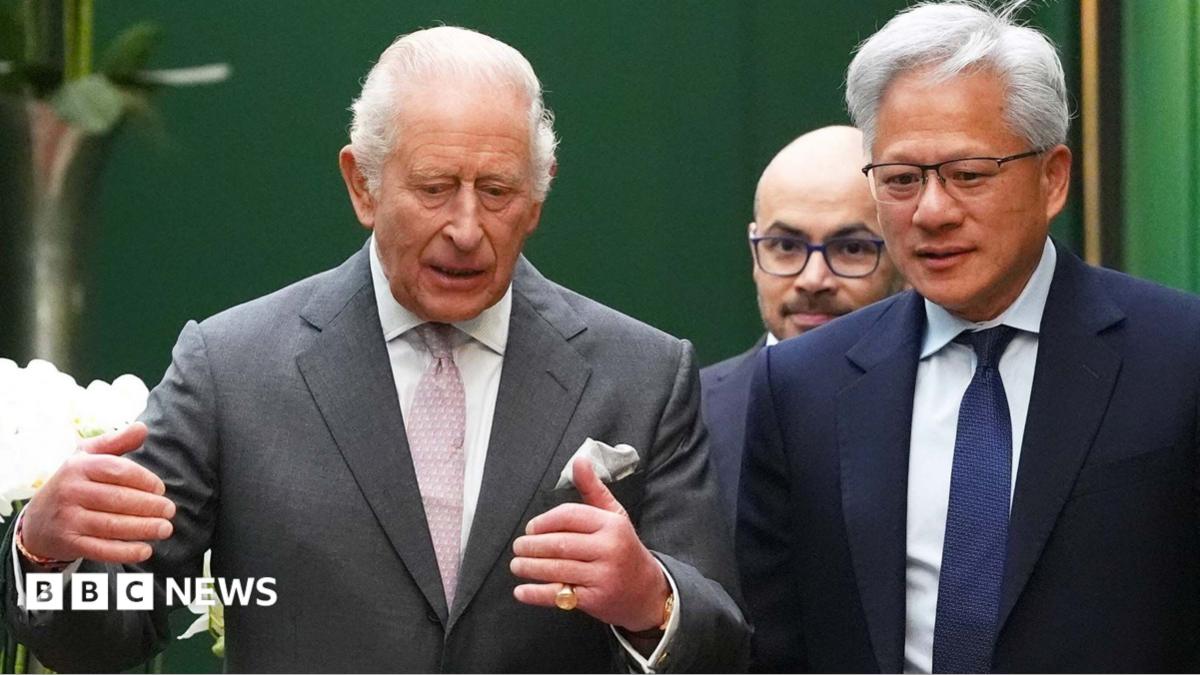 King Charles wearing a grey suit jacket and white shirt and pink tie, talking to Jensen Huang, the CEO of Nvidia, who is wearing a dark suit, white shirt and blue tie. Former Google DeepMind boss Sir Demis Hassabis is walking behind them.