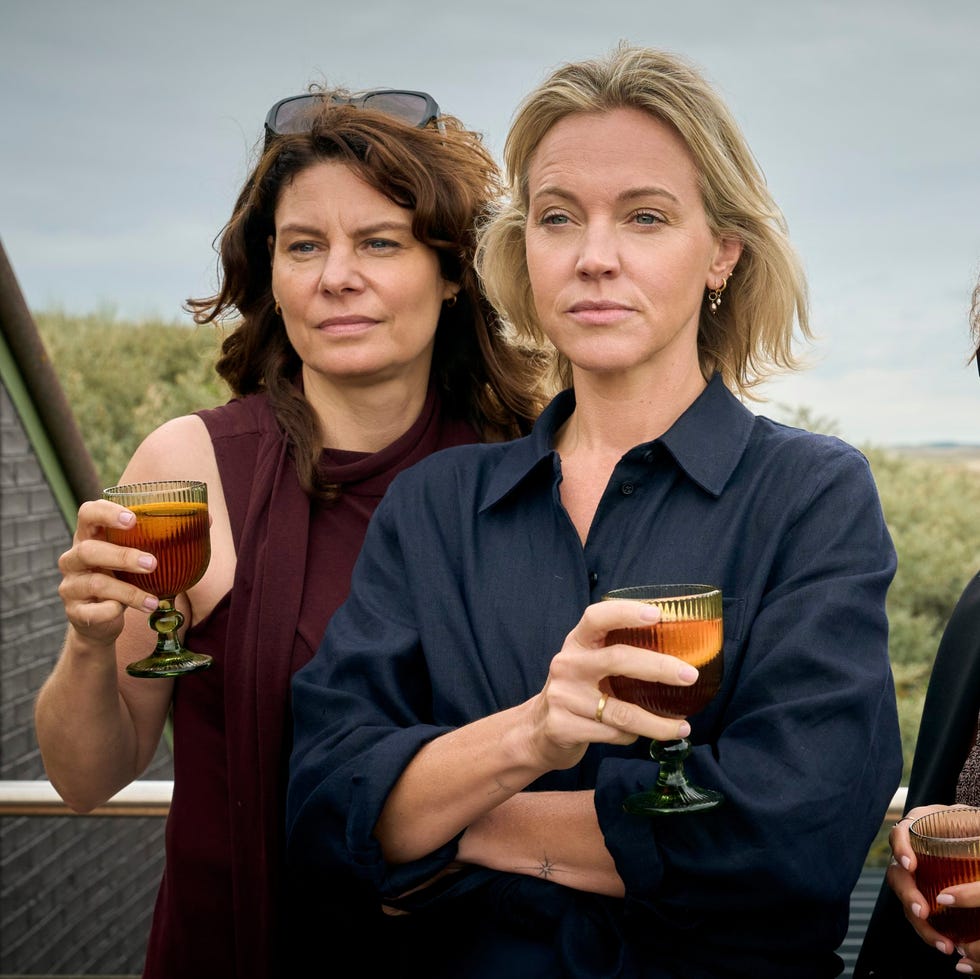 three women holding drinks outdoors with a cloudy sky.