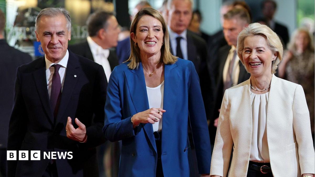 A smiling Mark Carney, wearing a suit, walks alongside European Parliament President Roberta Metsola and Ursula von der Leyen at the European Parliament