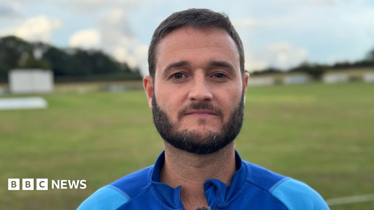 A man with black hair and beard, wearing a light blue tracksuit with a blue collar