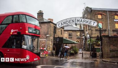 A red London bus heading to Camden Town passes by the entrance to Camden Market.