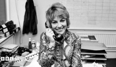 Esther Rantzen appears in a recent picture. She is smiling and dressed in a blue jacket with a matching feather in her hair.