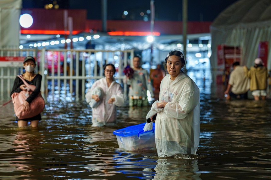 A woman drags a plastic tub as she wades though knee-high floodwater near a shopping centre.