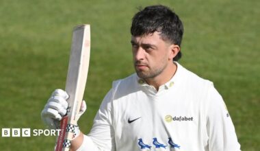 Tom Haines, helmet off, lists his bat in right hand