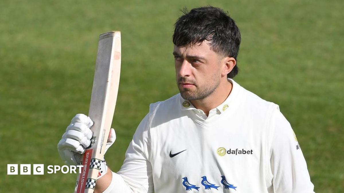 Tom Haines, helmet off, lists his bat in right hand
