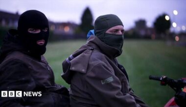 Two young men wearing balaclavas sit on a red quad bike