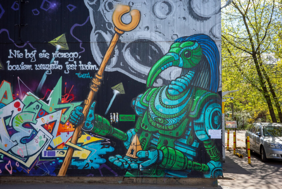 Colorful graffiti mural beside a tree-lined street with parked cars in Warsaw, Poland.