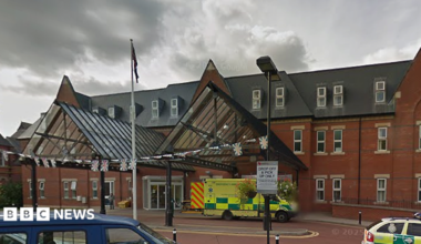 The entrance to Royal Albert Edward Infirmary in Wigan, Greater Manchester, on a cloudy day. An ambulance is parked at the entrance door and a paramedic vehicle seen to the right.