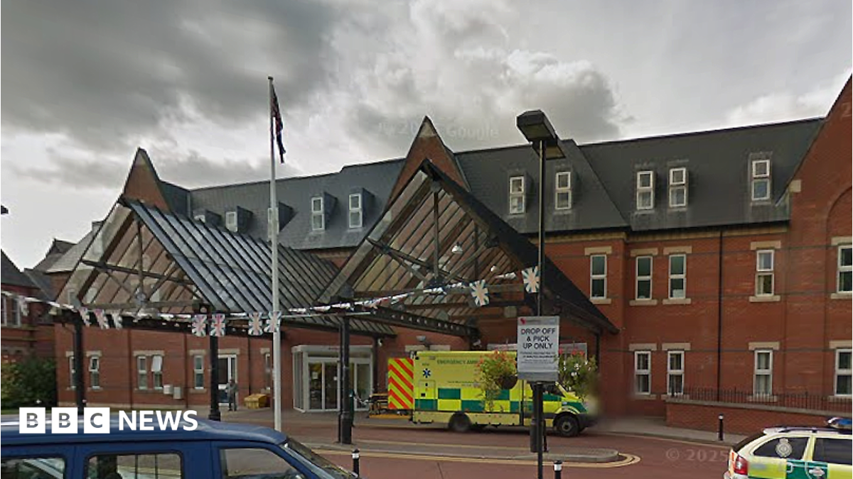 The entrance to Royal Albert Edward Infirmary in Wigan, Greater Manchester, on a cloudy day. An ambulance is parked at the entrance door and a paramedic vehicle seen to the right.