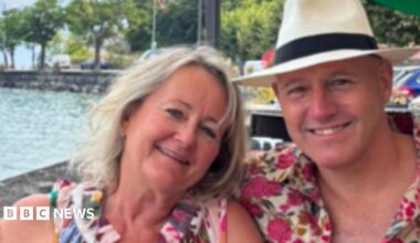 A couple on holiday wearing floral bright clothing smiling at the camera with their arms around one another