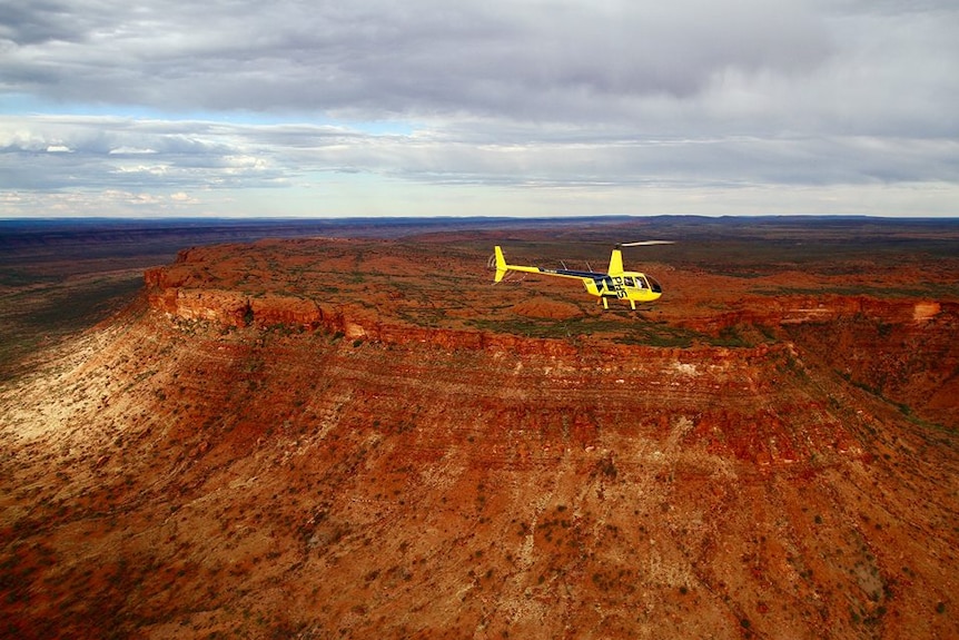 A helicopter flies above a spectaular outback landscape.