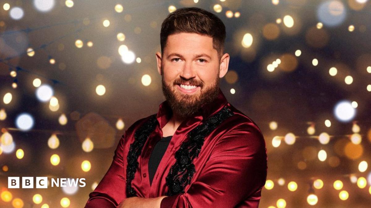 A promo image of a man and a woman dancing. They are both in red/burgundy flamboyant outfits and are smiling as they raise their arms.