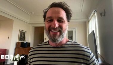 Actor Matthew Rhys sitting in room and wearing long sleeve t-shirt with grey and navy stripes