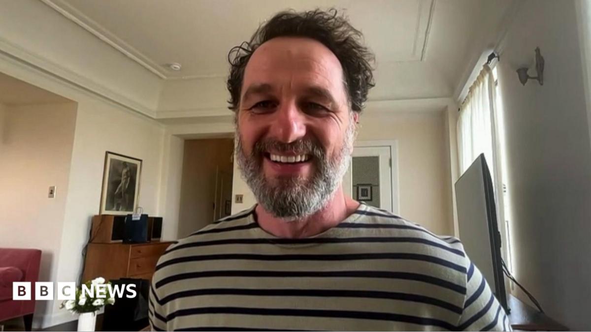 Actor Matthew Rhys sitting in room and wearing long sleeve t-shirt with grey and navy stripes