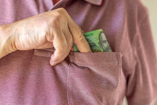 Close-up on a man’s hand taking a one hundred Australian dollar note into his shirt’s pocket.
