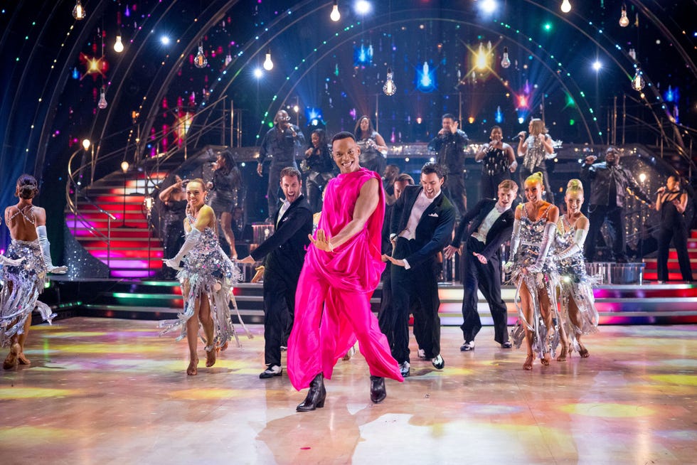 strictly come dancing 2026 johannes radebe dancers in colorful costumes performing on a stage with vibrant lights in the background.