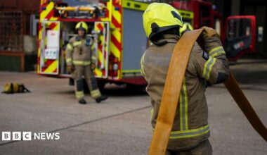Two firefighters working beside a fire engine. They are both in full protective gear.