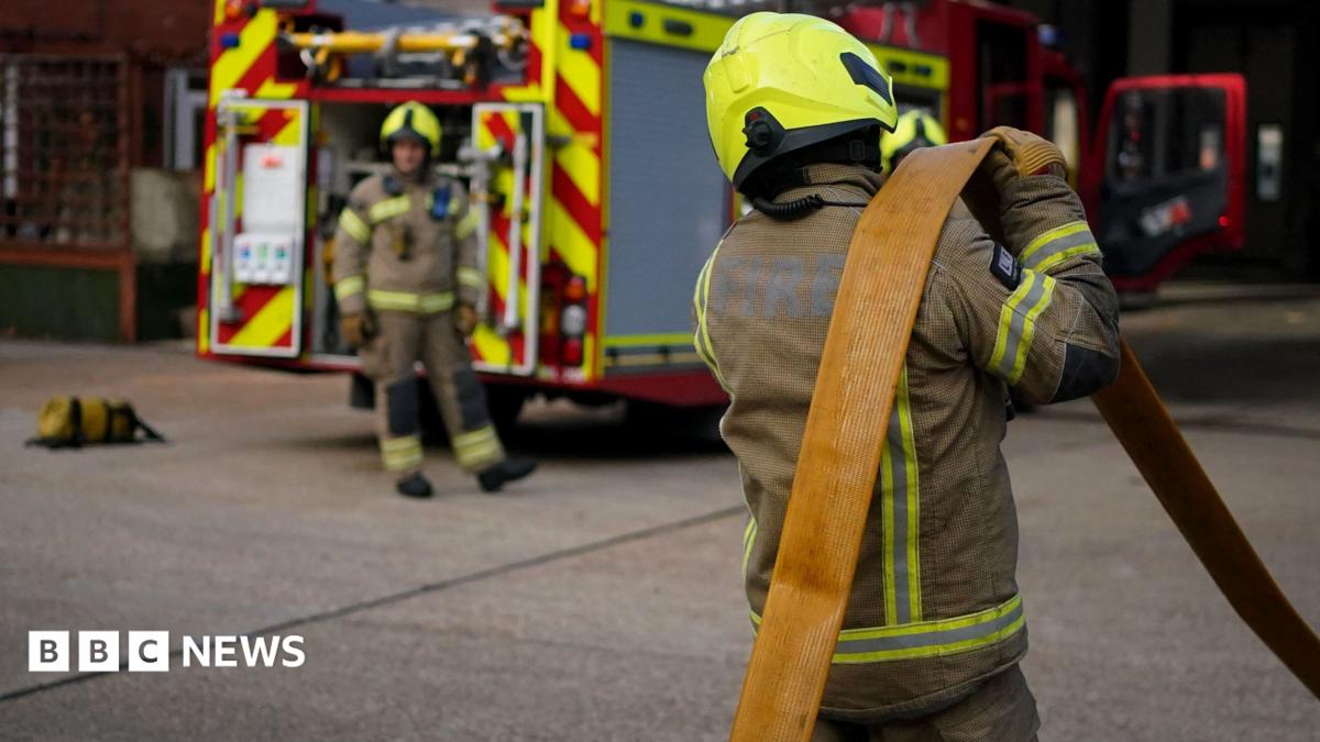 Two firefighters working beside a fire engine. They are both in full protective gear.