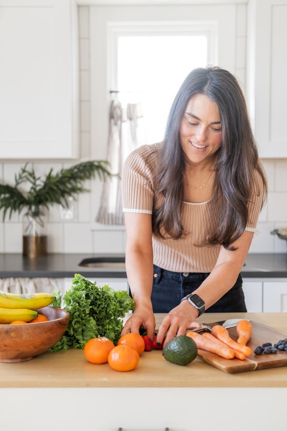 A woman preparing fresh fruits and vegetables in a bright kitchen.