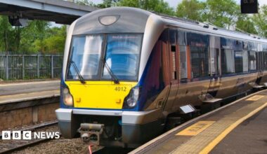 A train parked at a station. It is mostly blue and silver, and has a yellow box ohn the front.
