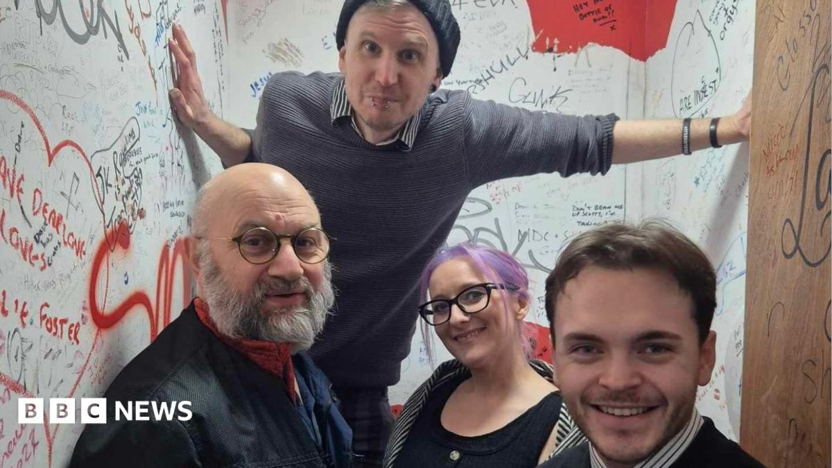 Four people stand in a small room with writing all over the walls.