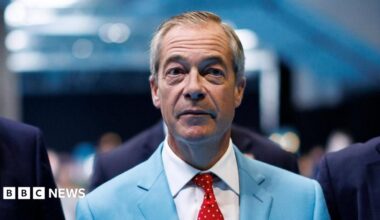 Reform UK leader Nigel Farage is wear a turquoise-coloured suit jacket, white shirt and a red tie with white dots.
