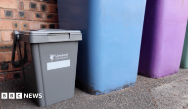 A small grey plastic bin with Liverpool City Council written on it stands next to taller blue and purple bins