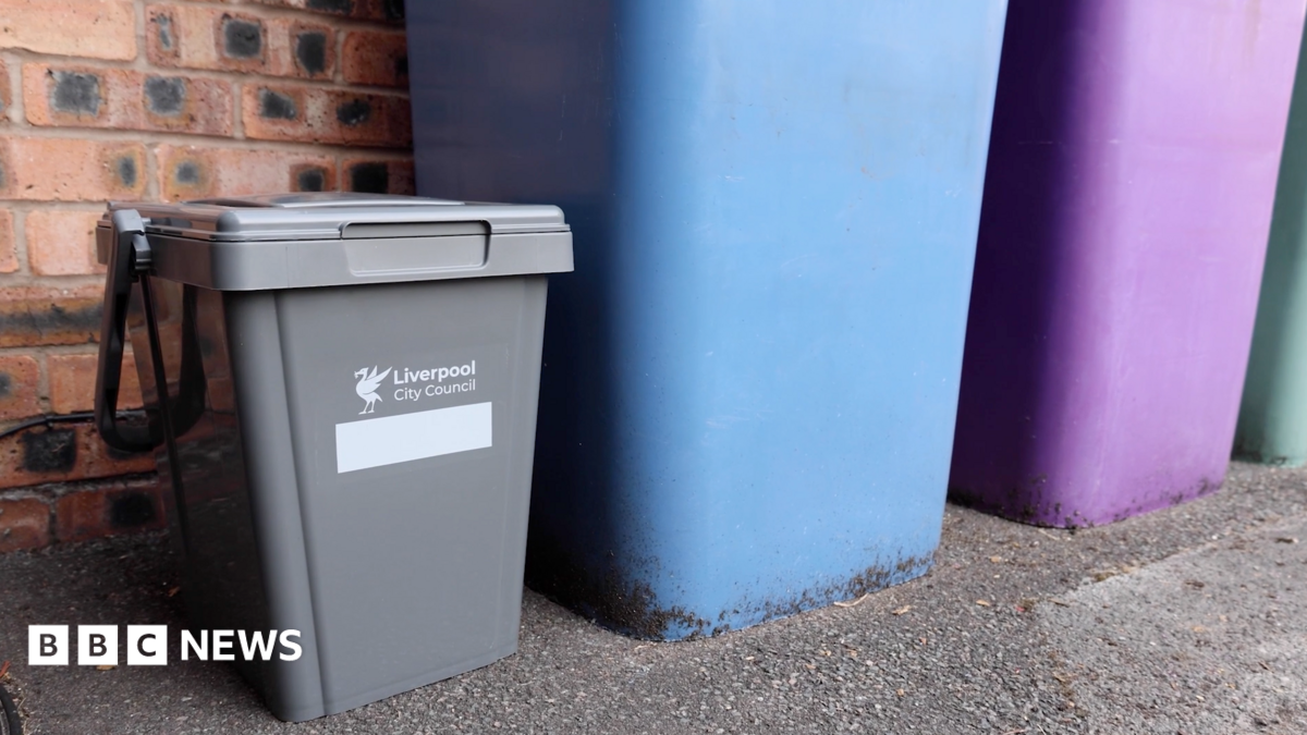 A small grey plastic bin with Liverpool City Council written on it stands next to taller blue and purple bins