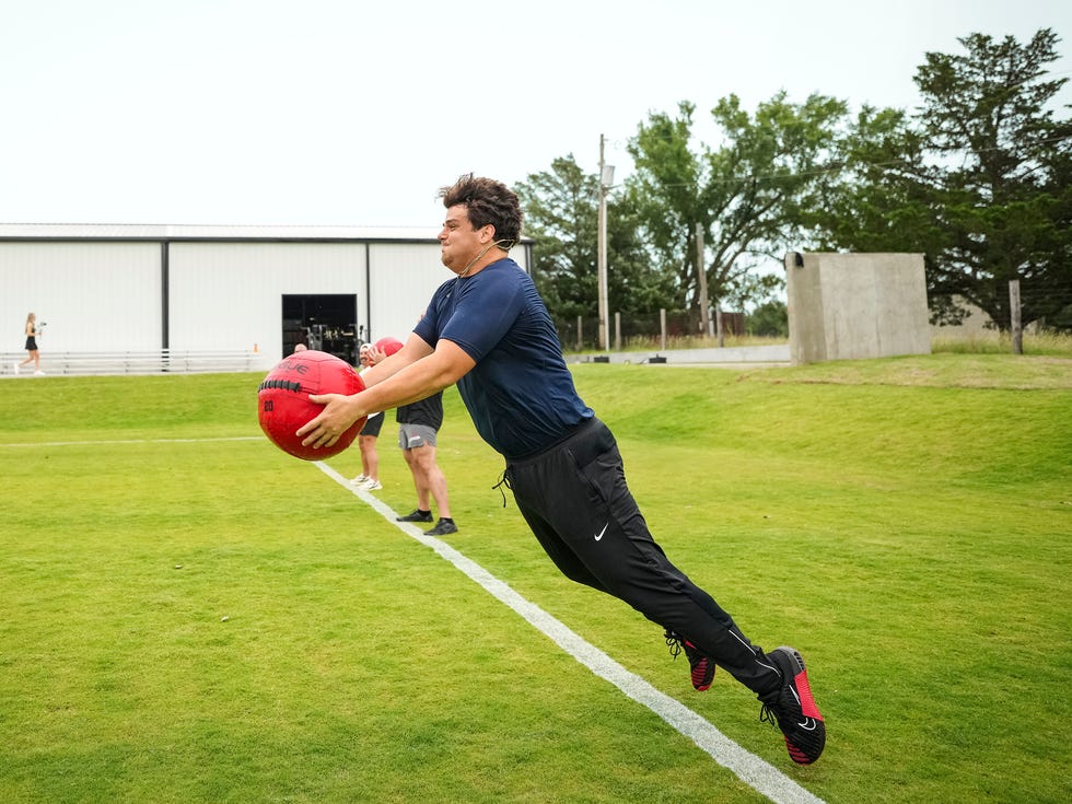 Man jumping while throwing a red medicine ball on a grass field with a building in the background. Man jumping while throwing a red medicine ball on a grass field with a building in the background.