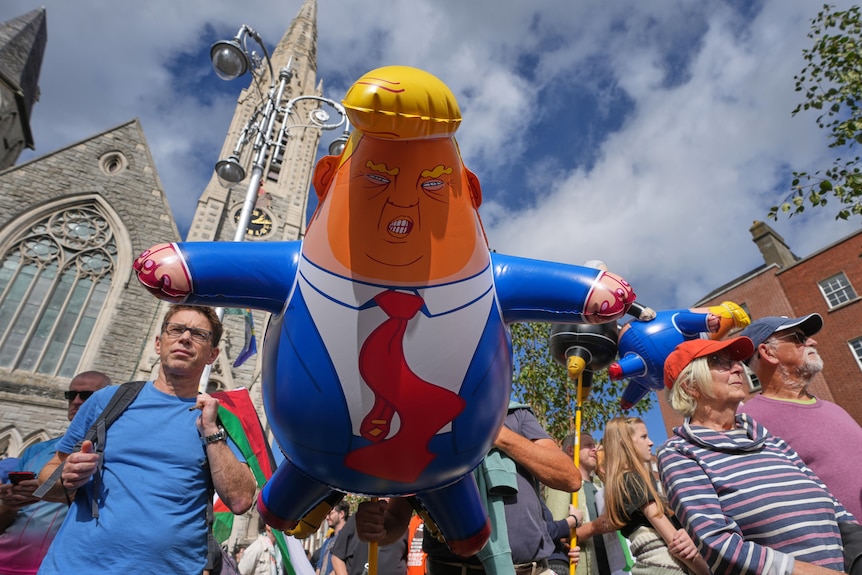 A balloon in the shape of Donald Trump floats among protesters.