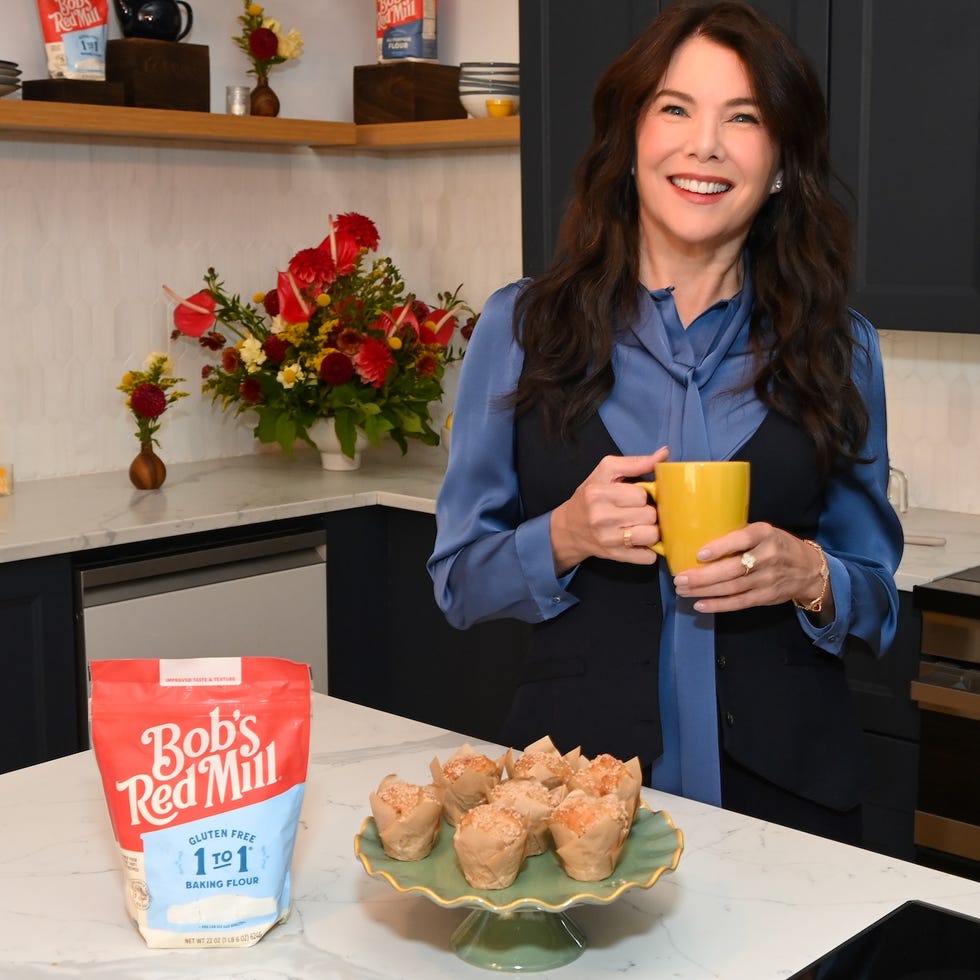 Woman in a kitchen holding a yellow mug, smiling beside a platter of baked goods and a bag of Bob's Red Mill flour. Woman in a kitchen holding a yellow mug, smiling beside a platter of baked goods and a bag of Bob's Red Mill flour.