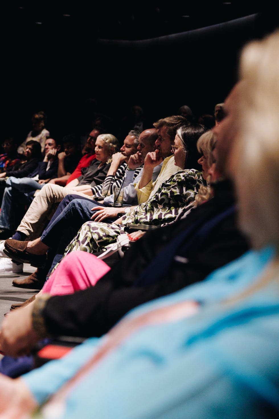 audience seated in a dimly lit venue, attentively watching a presentation.