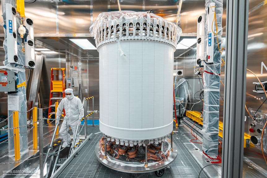 A big white tank with a person in full clean room gear behind it. 
