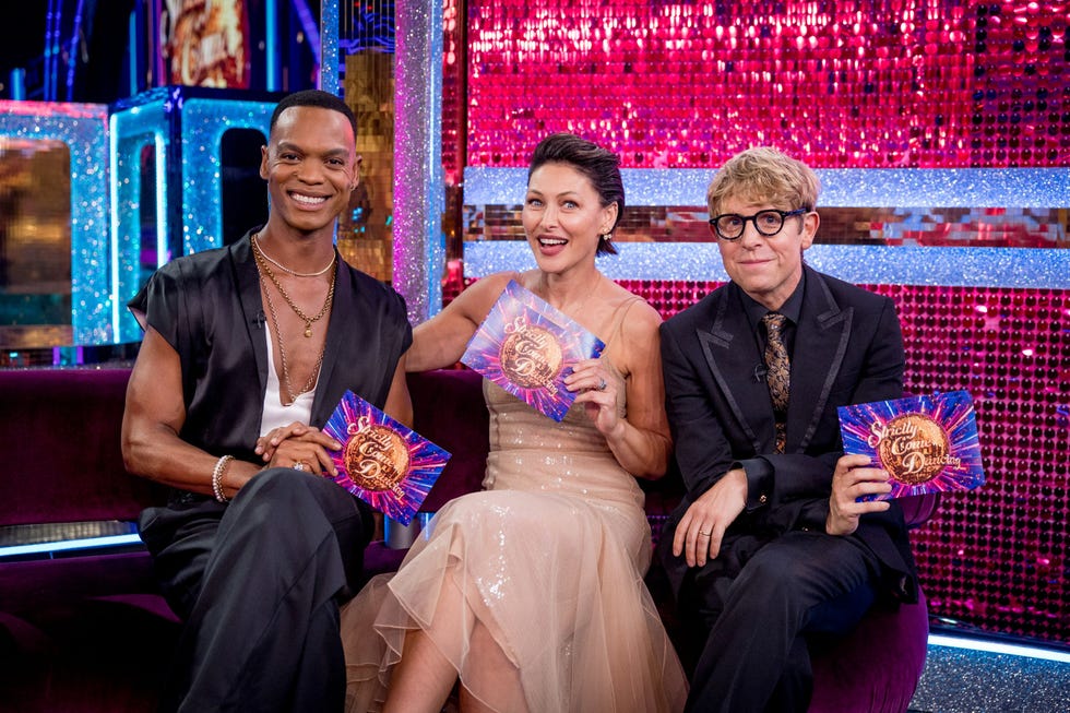 strictly come dancing johannes radebe emma willis josh widdicombe three people sitting on a couch, holding "strictly come dancing" cards, with a sparkling background.