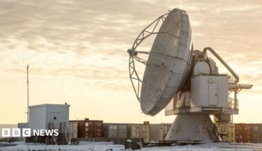 The Pituffik Space Base (formerly Thule Air Base) is pictured in northern Greenland, on October 4, 2023. It shows a large satelitte dish in front of containers, with a cloudy orange sky in the background.