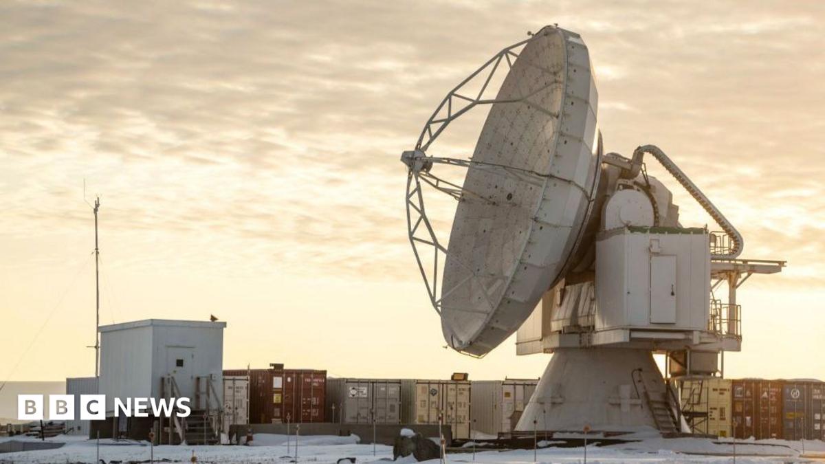The Pituffik Space Base (formerly Thule Air Base) is pictured in northern Greenland, on October 4, 2023. It shows a large satelitte dish in front of containers, with a cloudy orange sky in the background.