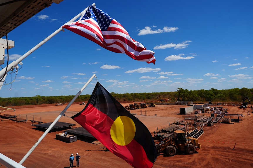 An Aboriginal flag flying alongside the United States of America flag over a red dirt landscape covered in mining equipment.