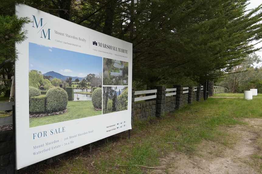 A white For Sale sign sits in front of a bluestone fence.