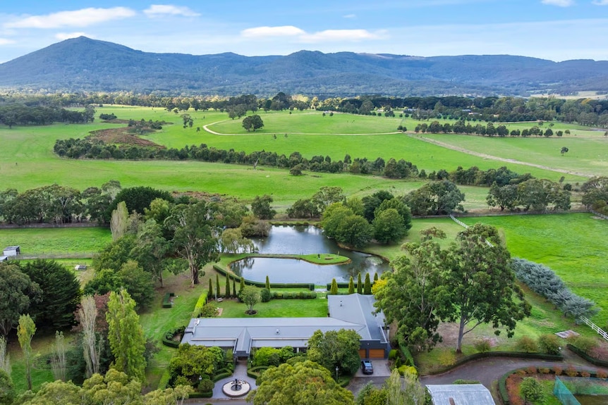 An aerial photo shows an expansive residential property surrounded by greenery with mountains in the background.