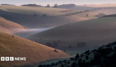 A series of slopes overlooking a valley with mist at the bottom. Trees are dotted around the landscape.