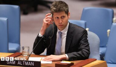 Sam Altman of OpenAI sitting before the US Security Council wearing a suit and tie while listening to a translation of comments.