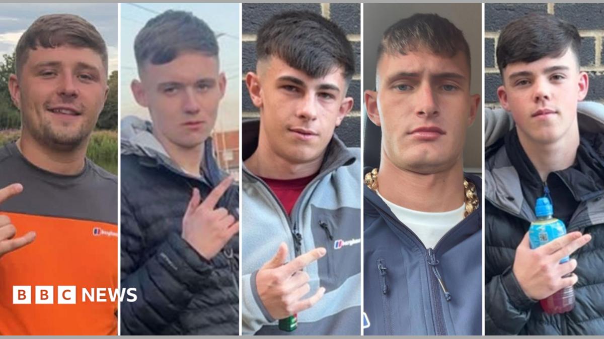 Five young men in their late teens and early 20s. They all have similar haircuts, with a fringe and faded back and sides. Four of them are gesturing with their fingers. Three of them extend their thumb, index, and pinky fingers - leaving their middle and ring finger tucked down. One points with his index and middle finger whilst holding a Lucozade bottle. They are all dressed in casual clothing.