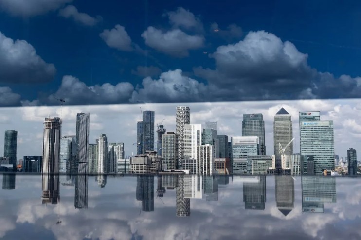 London financial district skyscrapers reflecting in water, under a dramatic cloudy sky