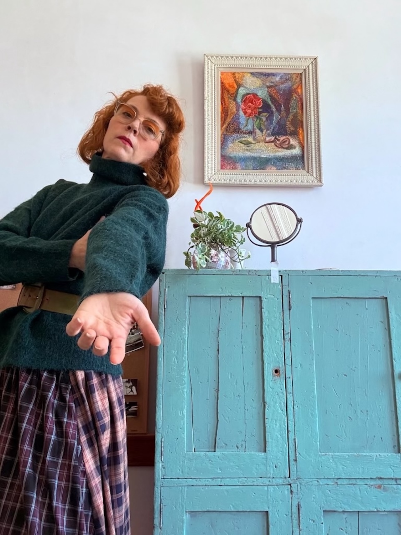 Melissa Auf Der Mar stands in a green sweater and plaid skirt. She holds open her palm to the camera.