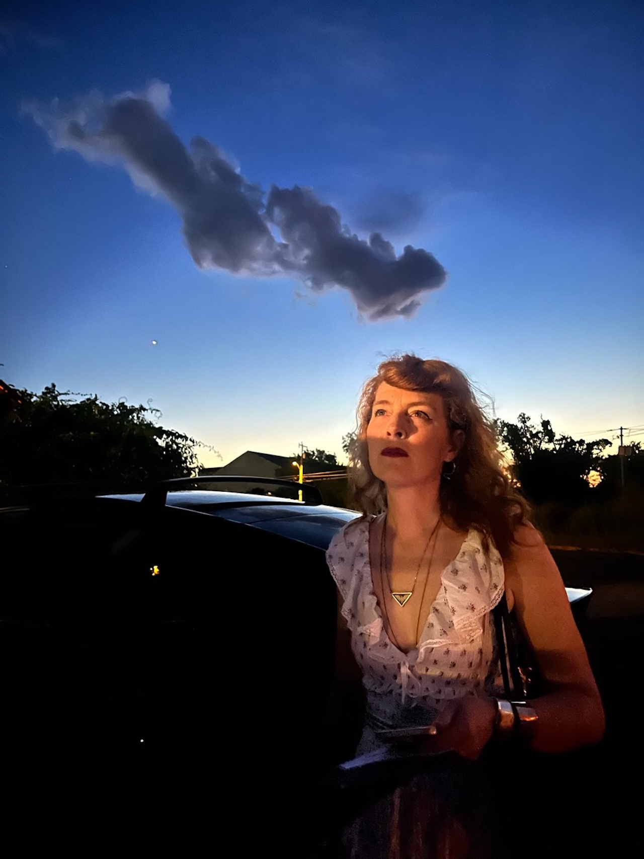 Melissa Auf Der Mar stands under a blue sky at night looking up toward the clouds.