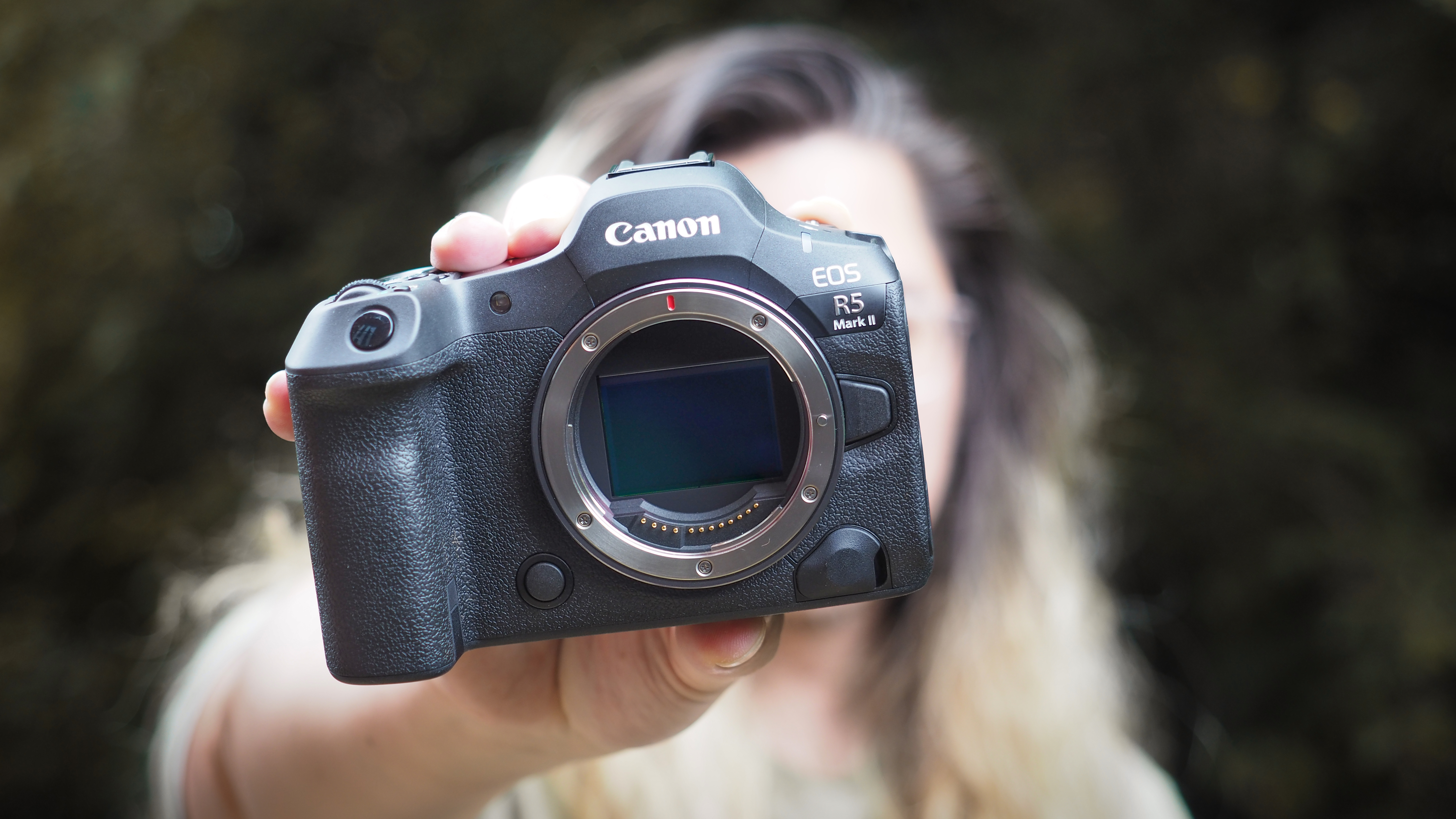 Canon EOS R5 Mark II being held out in front of a photographer's face, outdoors