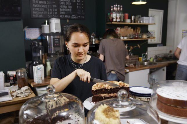 A waitress in a cafe cutting a slice of cake for a customer / Female Focus Collection