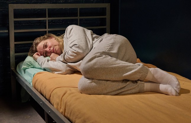 Charity Dingle, wearing a grey sweatsuit, curled up on her bed in the prison cell in Emmerdale. She looks desperately sad.